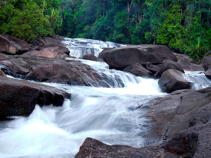 Upeh Guling waterfall flows between large rocks in the rainforest at Endau-Rompin Peta.